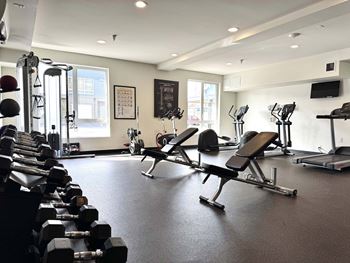 A gym with a variety of equipment including dumbbells, weight benches, and treadmills.